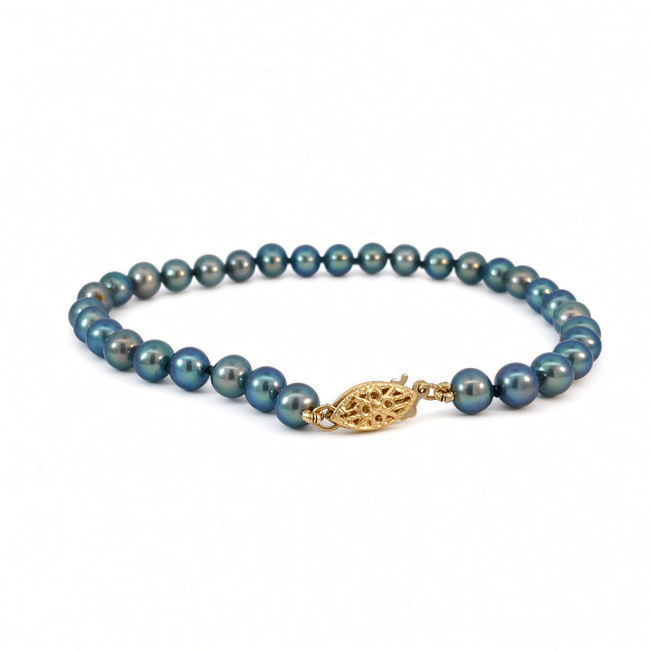 A beaded necklace featuring dark teal-blue pearls with a textured gold leaf-shaped clasp