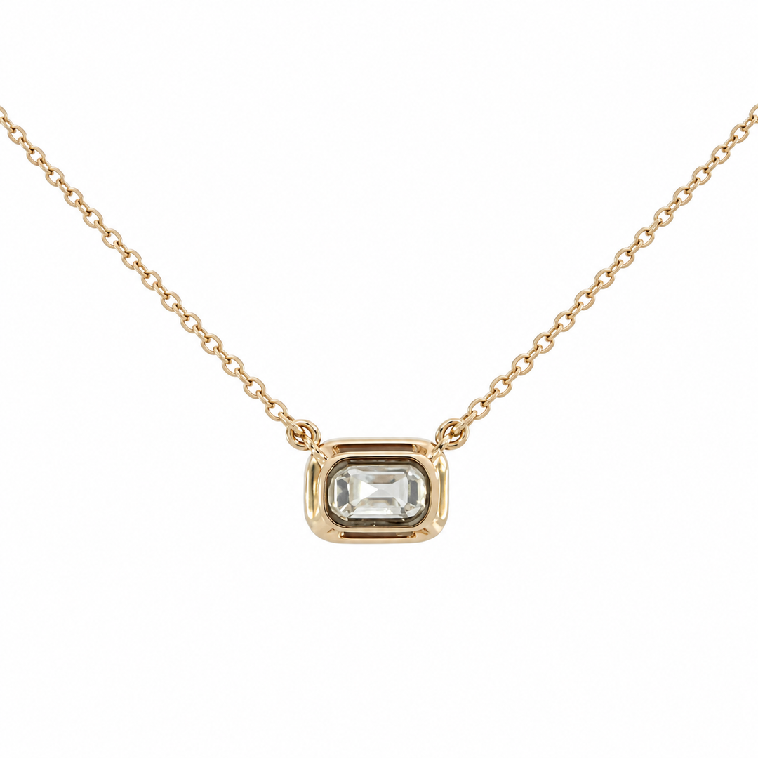 A delicate gold chain necklace featuring a rectangular bezel-set clear gemstone pendant, 
