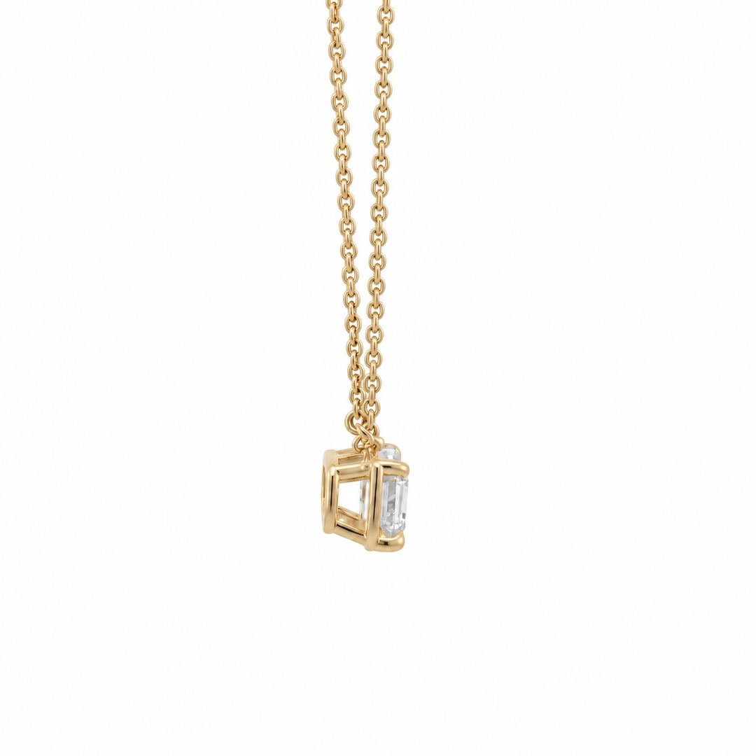 A gold chain necklace with a geometric cube pendant featuring a clear emerald cut diamond