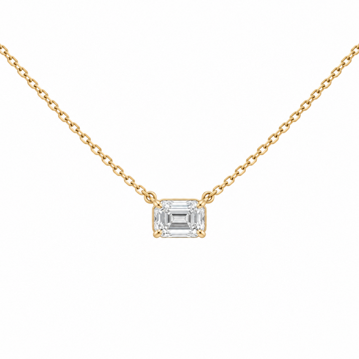 A delicate yellow gold chain necklace featuring an emerald-cut clear gemstone pendant in a four-prong setting,