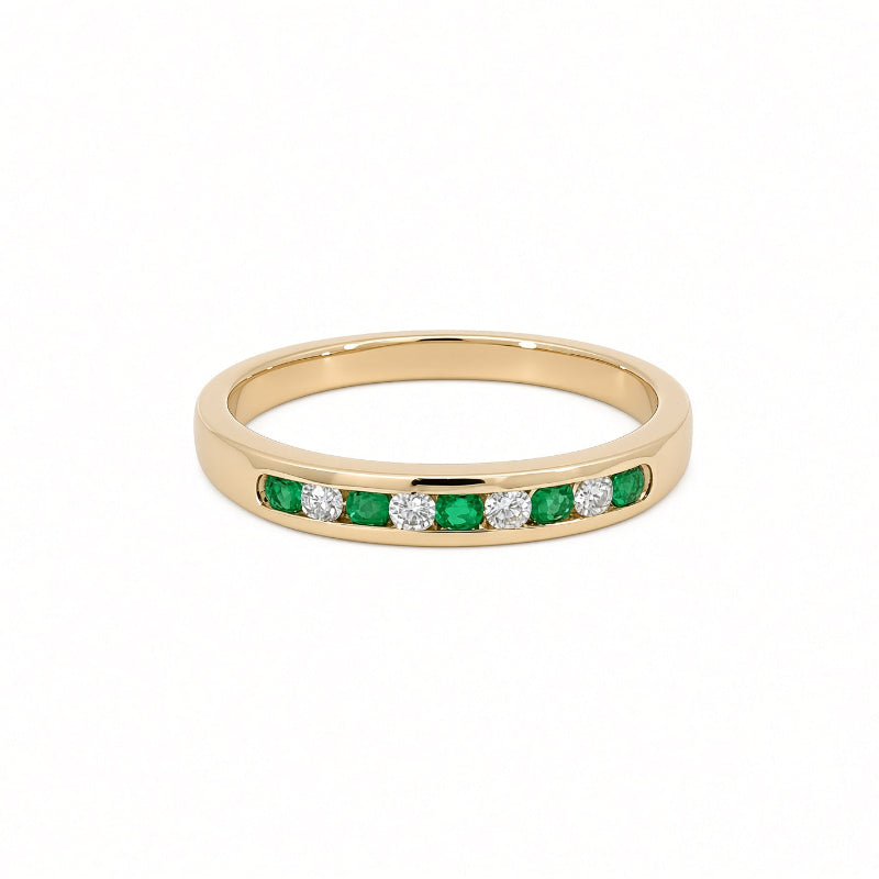 A yellow gold ring featuring a channel-set row of round-cut green emeralds and round-cut clear diamonds