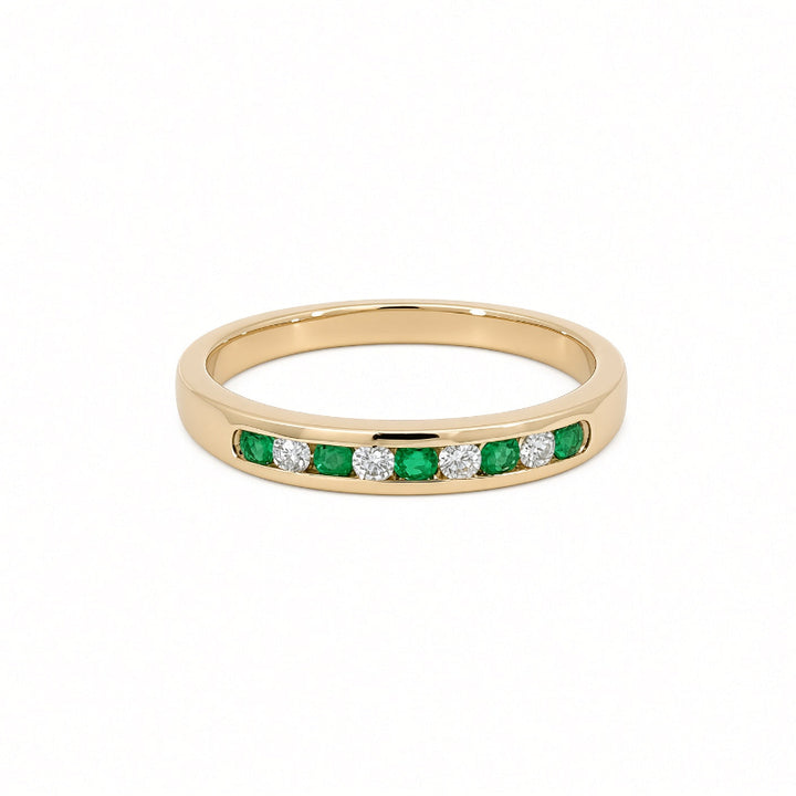 A yellow gold ring featuring a channel-set row of round-cut green emeralds and round-cut clear diamonds