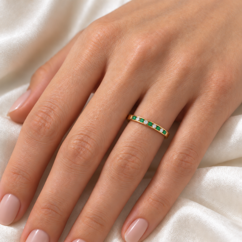 A delicate gold band ring with a row of small green and white stones
