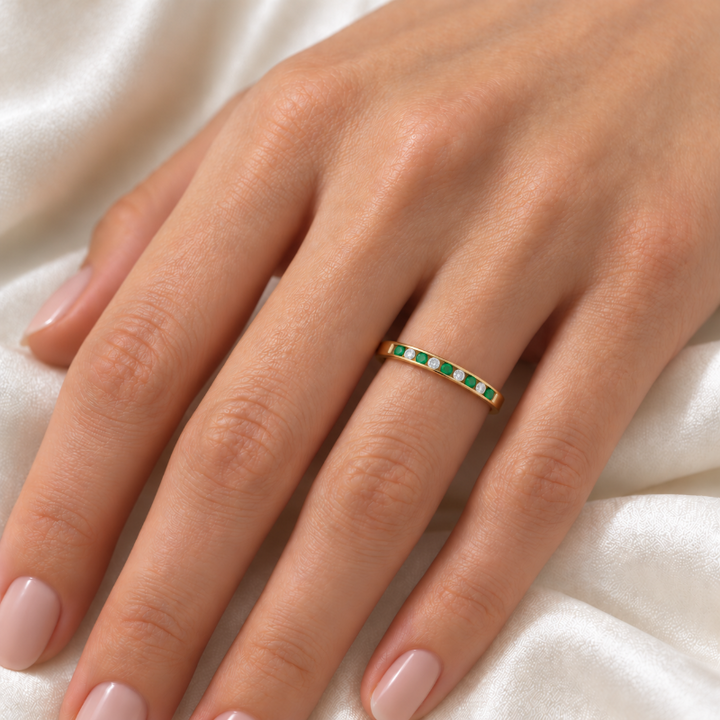 A delicate gold band ring with a row of small green and white stones